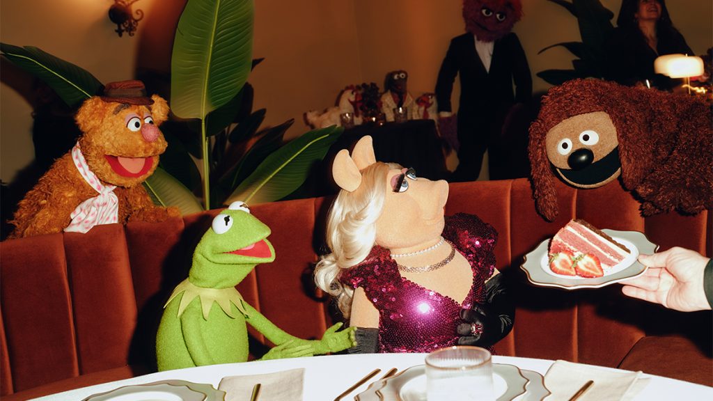 Two images side by side, from the Muppet Show premiere event at the Hollywood Roosevelt in Los Angeles on January 31, 2026. On the left, Miss Piggy is looking out of a limousine window as camera flashes go off; she is raising sunglasses above her eyes. On the right, Kermit and Miss Piggy sit at a table booth and are being offered a slice of strawberry pie; behind them, Fozzie Bear (to Kermit&rsquo;s left) and Rowlf the Dog (to Miss Piggy&rsquo;s right) look on. There are various place settings and a white tablecloth on the table.