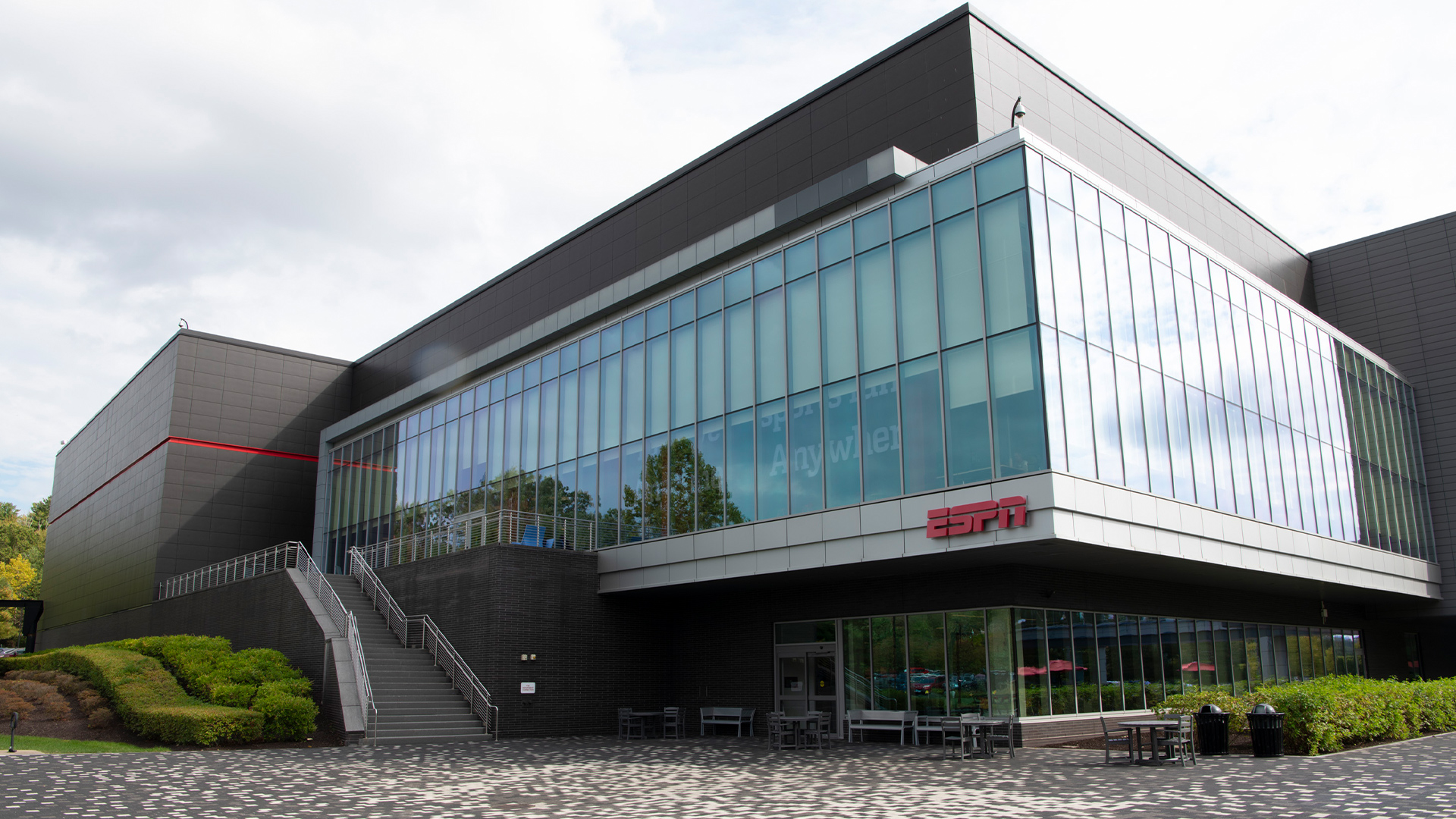 Modern glass-fronted ESPN building with red ESPN logo and outdoor seating area during a D23 ESPN tour.
