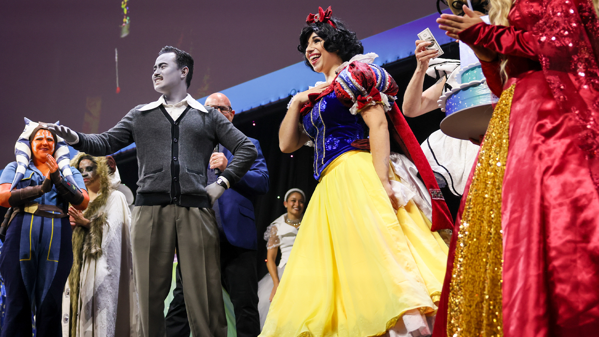 Fans dressed as Disney and Star Wars characters, including Snow White and Ahsoka Tano, gather on stage during a cosplay contest.
