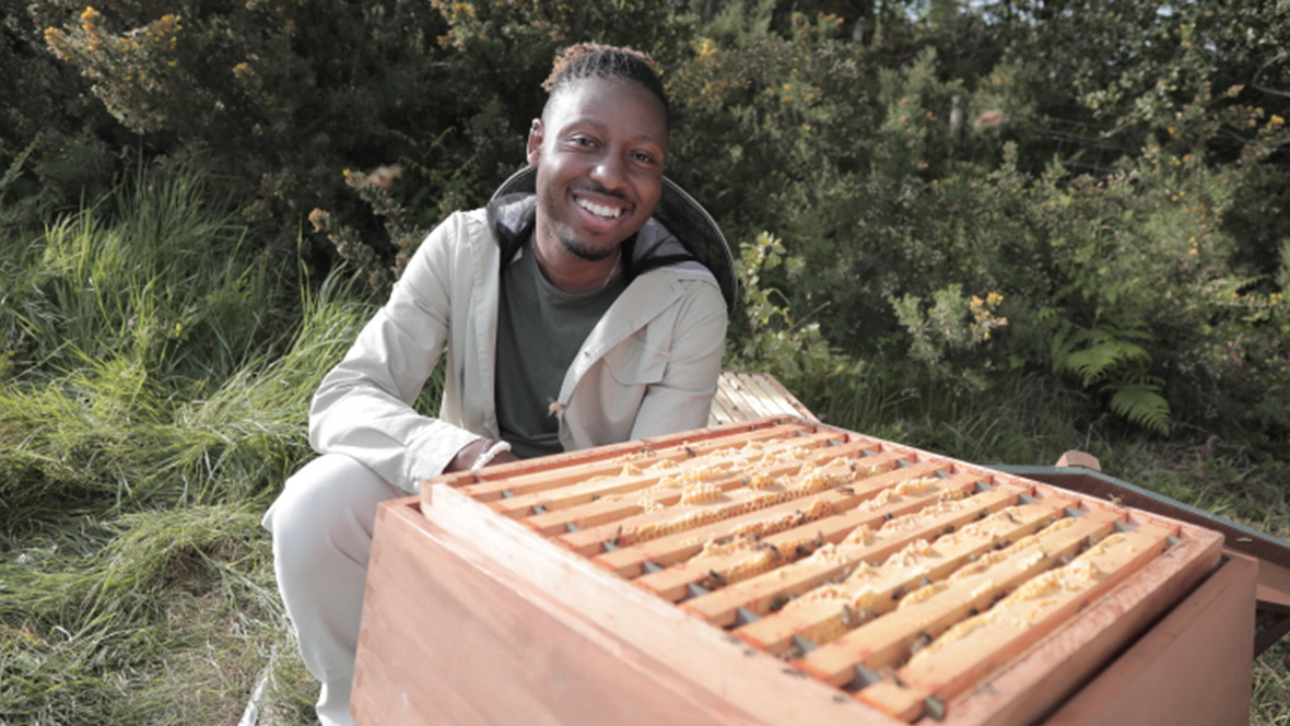 An image of entomologist and National Geographic Explorer Dr. Samuel Ramsey during filming of Nat Geo&rsquo;s Secrets of the Bees. He is crouching down near a wooden beehive box.