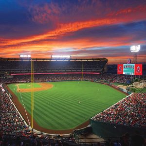 Fans watch a baseball game at Angel Stadium as the scoreboard displays the Los Angeles Angels logo and name at sunset.