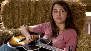 An image from Hannah Montana: The Movie, starring Disney Legend Miley Cyrus. Cyrus is holding an acoustic guitar.