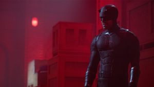 An image from Daredevil: Born Again season 2, featuring Charlie Cox as Daredevil. He is in his Daredevil suit and standing in front of stacked boxes.