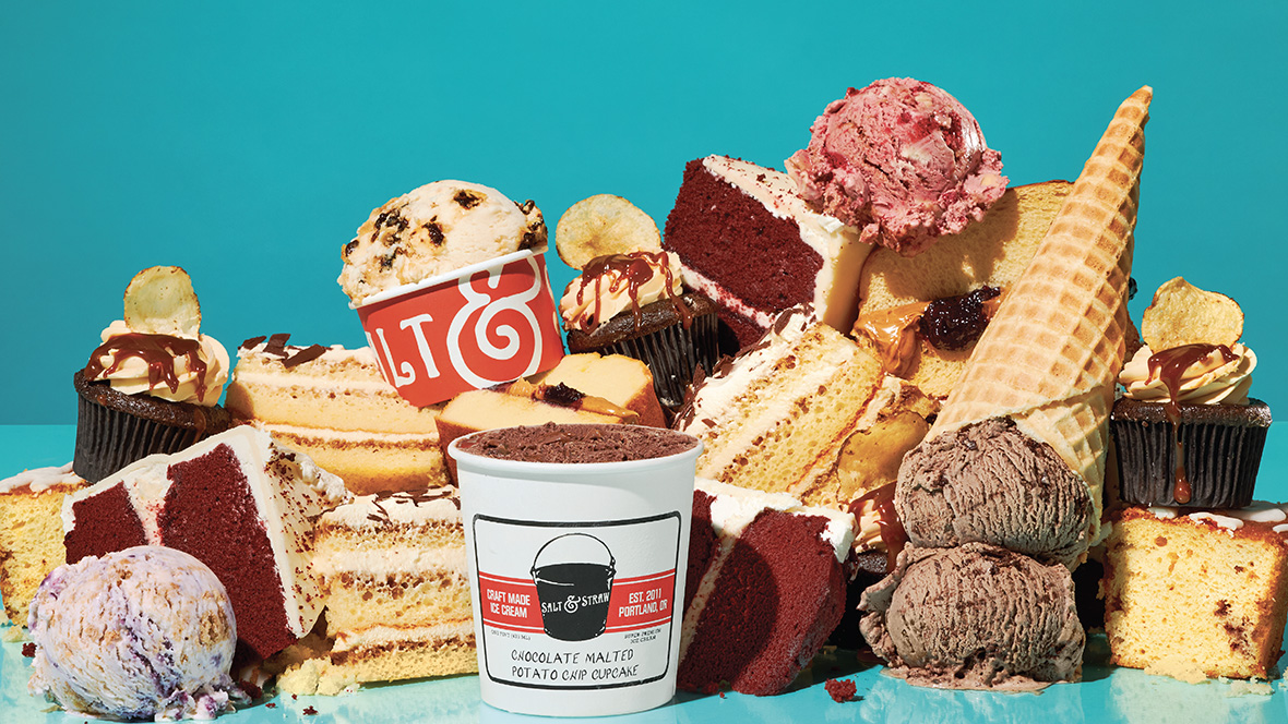 Several Salt & Straw ice cream scoops and cones are arranged among slices of cake and cupcakes against a blue background.
