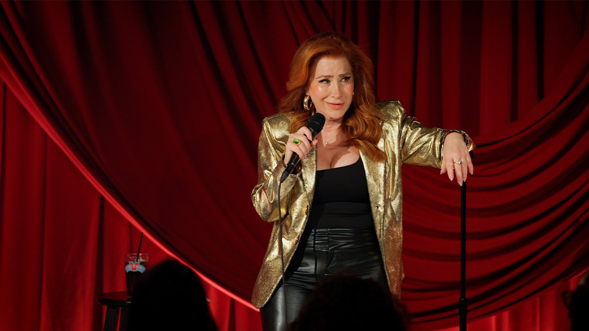 In an image from the new Hulu comedy special Lisa Ann Walter: It Was an Accident, actress and comedian Walter stands on stage, one hand holding a mic and the other arm resting on the mic stand. She&rsquo;s wearing a gold lam&eacute; blazer.