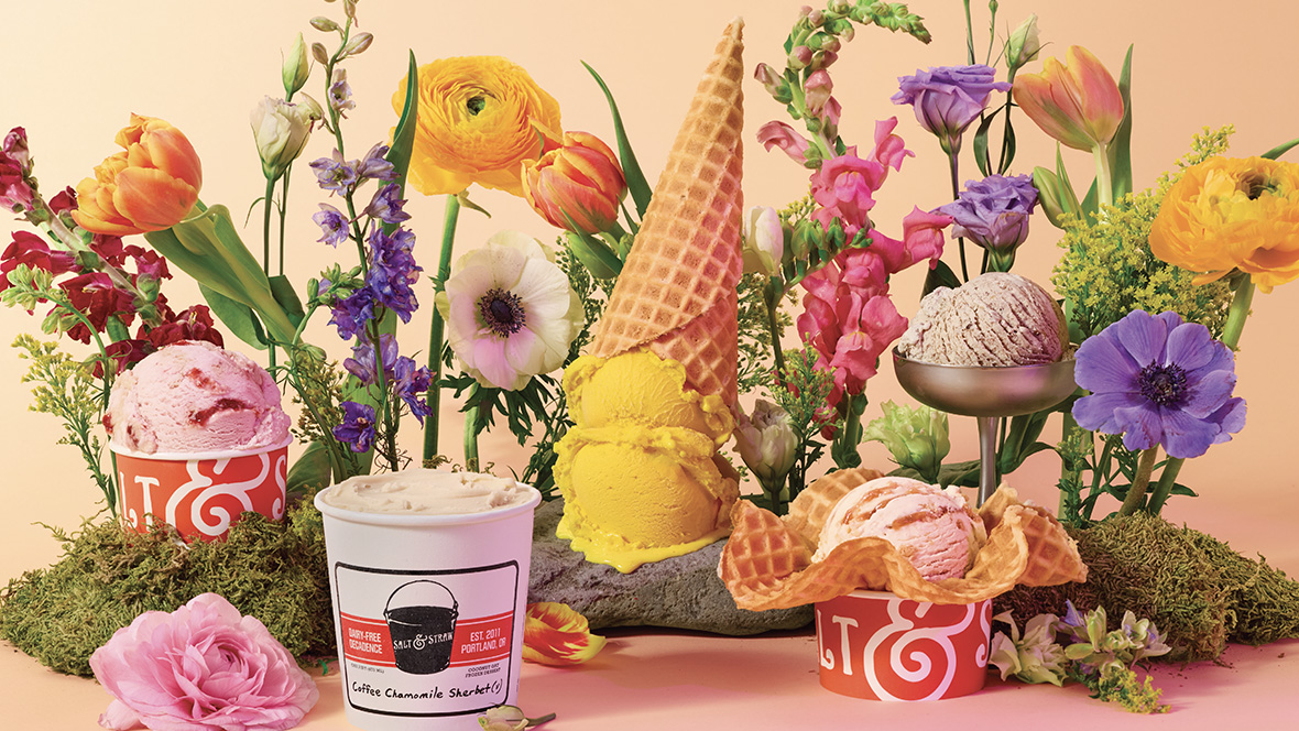 Several Salt & Straw ice cream scoops and cones are arranged among flowers with an orange background.