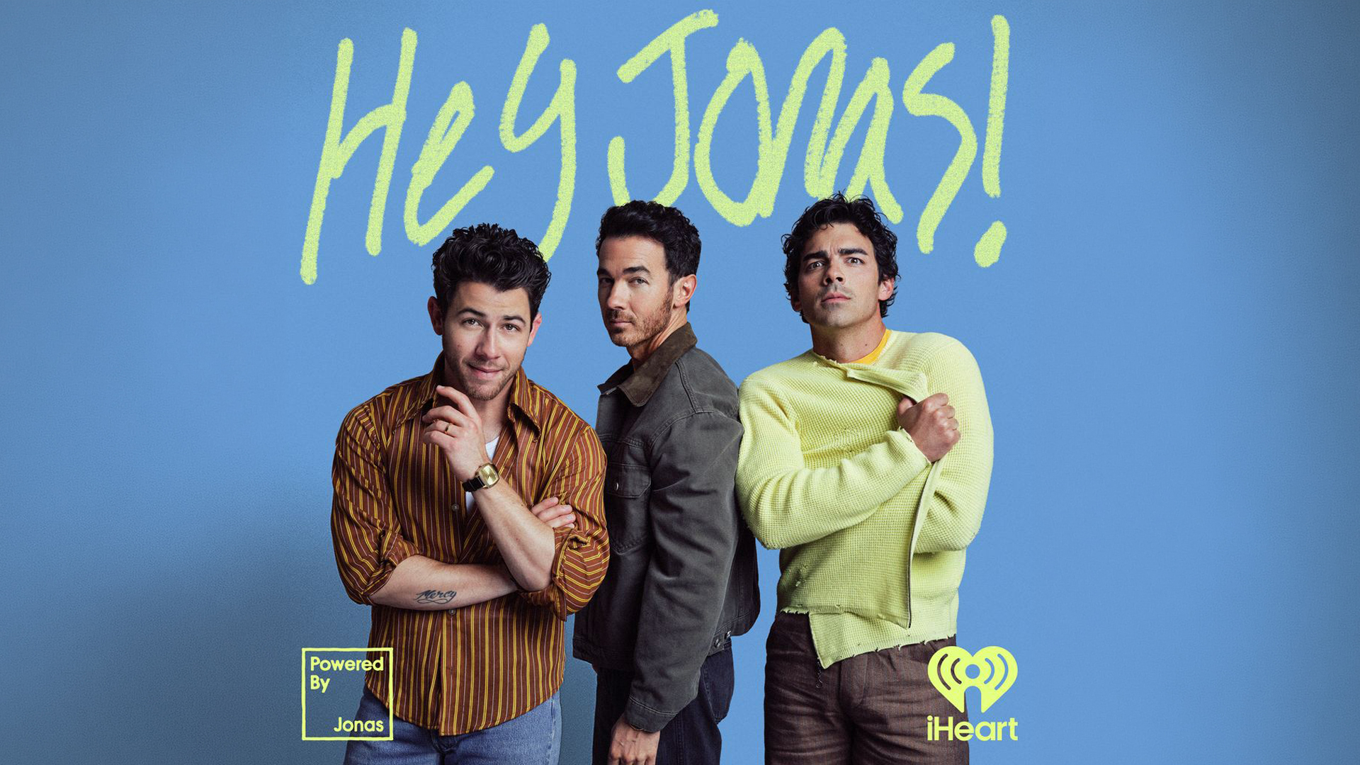 The Jonas Brothers stand together posing in front of a blue background with "Hey Jonas!" written above and iHeart logo visible.