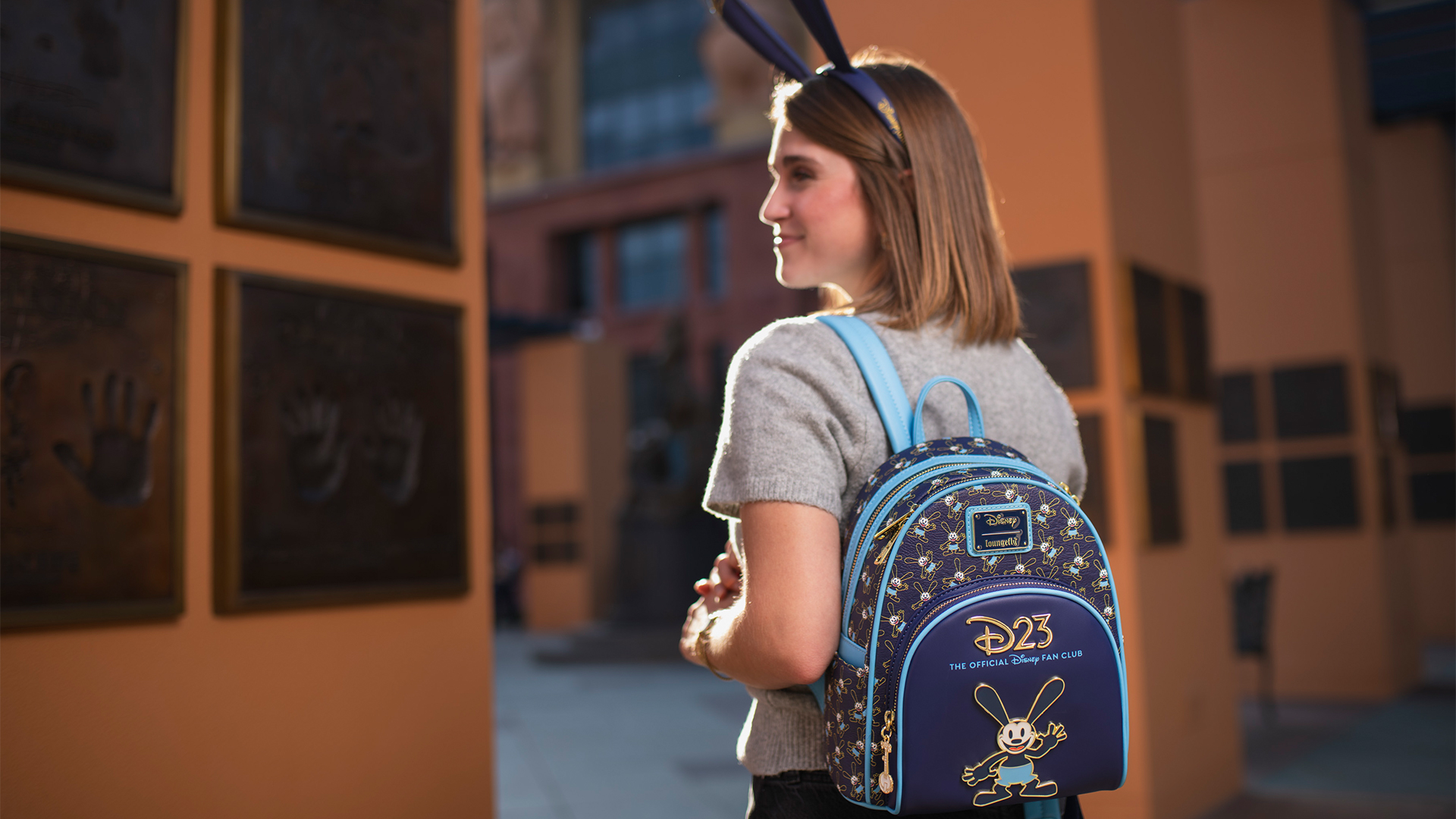 Alt-text: A person wears a blue D23 backpack featuring Oswald the Lucky Rabbit and &ldquo;D23 The Official Disney Fan Club&rdquo; branding.