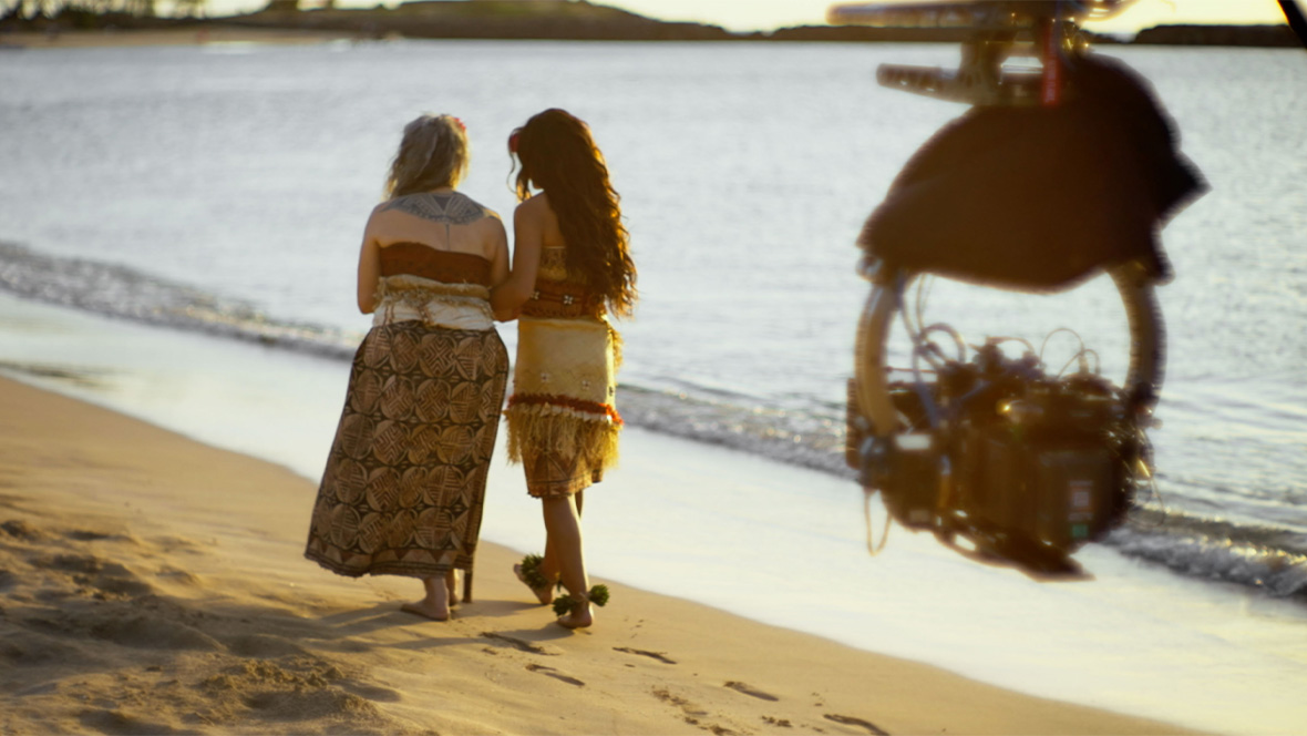 A behind-the-scenes image of Rena Owen as Gramma Tala and Catherine Lagaʻaia as Moana in Disney&rsquo;s live-action reimagining of the Oscar-nominated animated adventure Moana; the pair are walking along the beach.