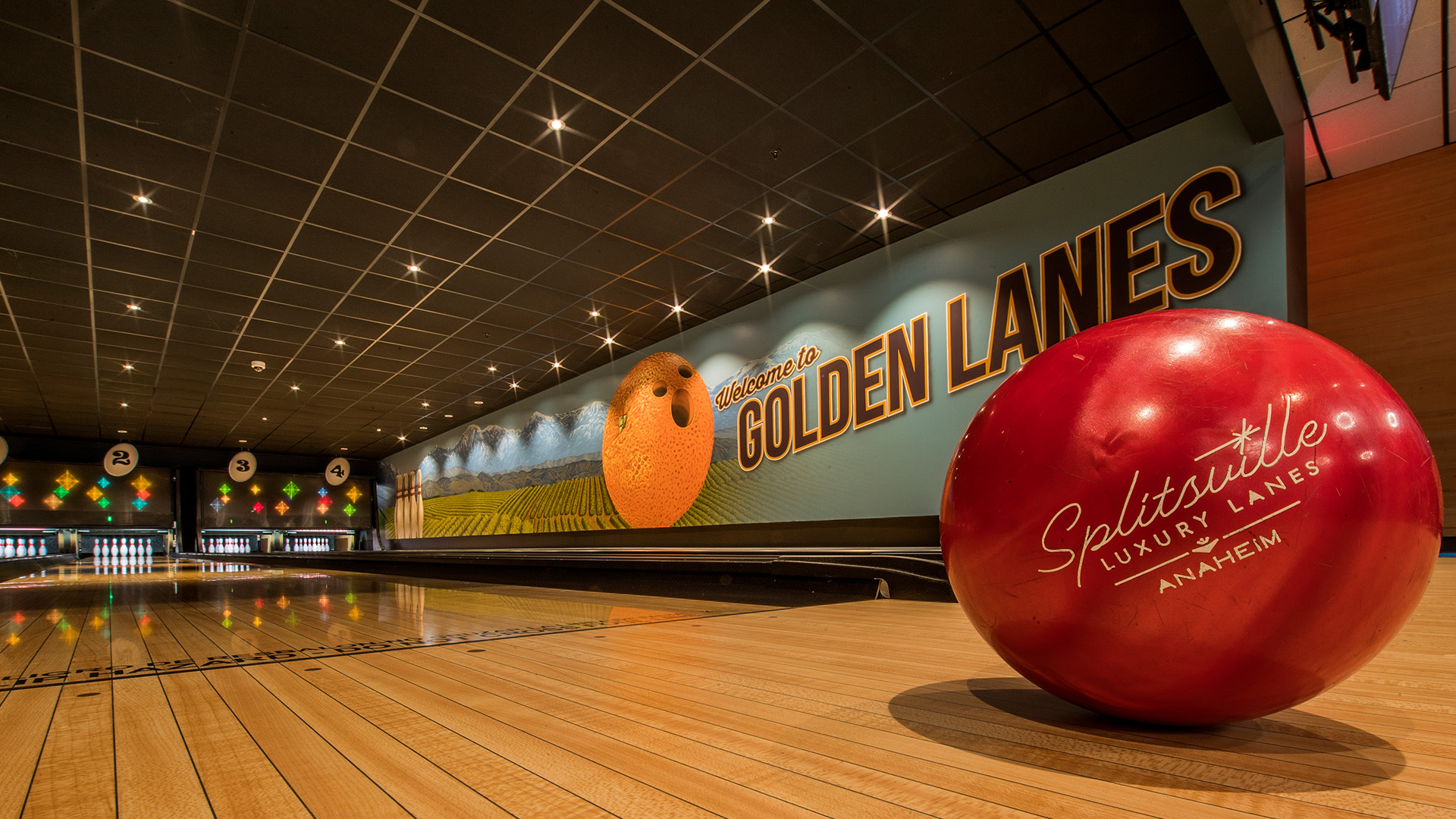 Red bowling ball sits beside polished lanes at Splitsville Luxury Lanes Anaheim beneath a large &ldquo;Welcome to Golden Lanes&rdquo; mural.
