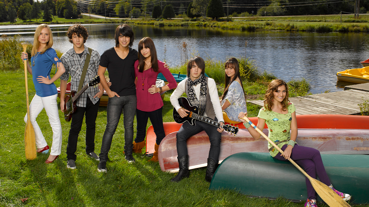 The cast of Camp Rock poses for a promotional photo by a lake.