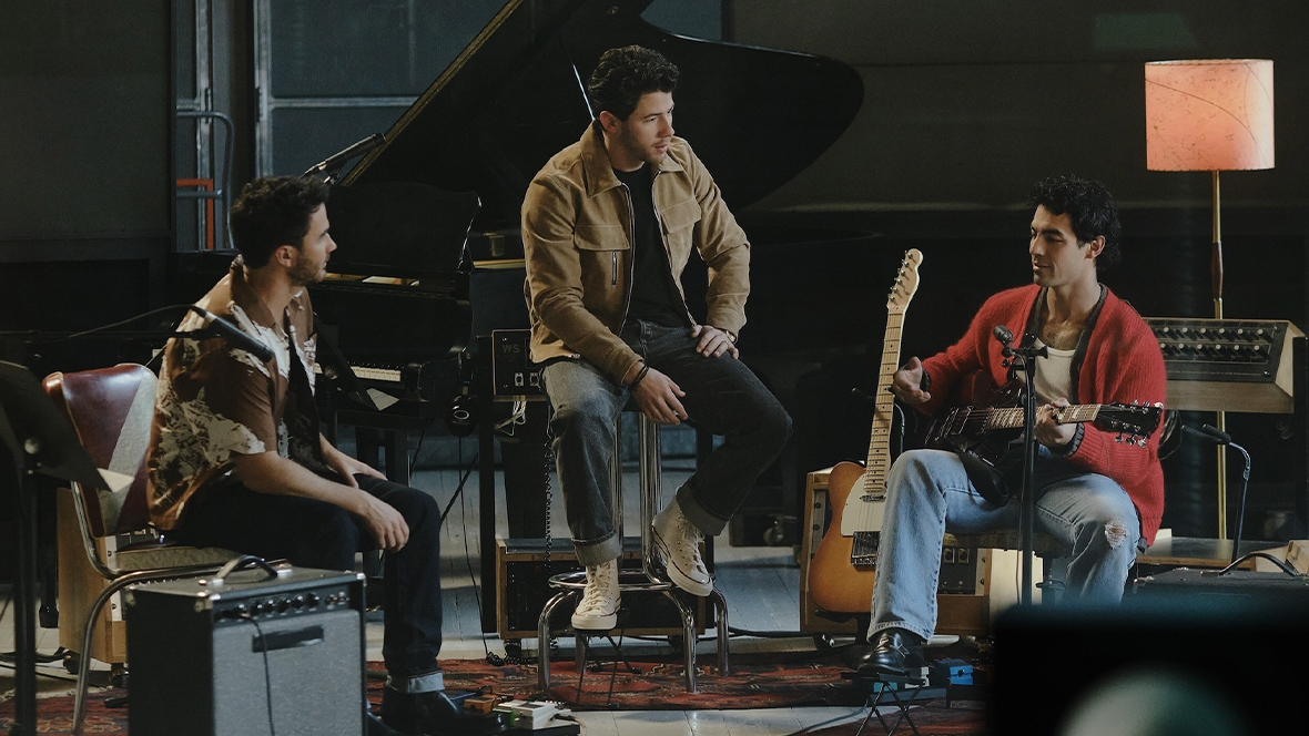 Disney Legends Kevin Jonas, Nick Jonas, and Joe Jonas chat in a rehearsal studio filled with instruments in a scene from Camp Rock 3.