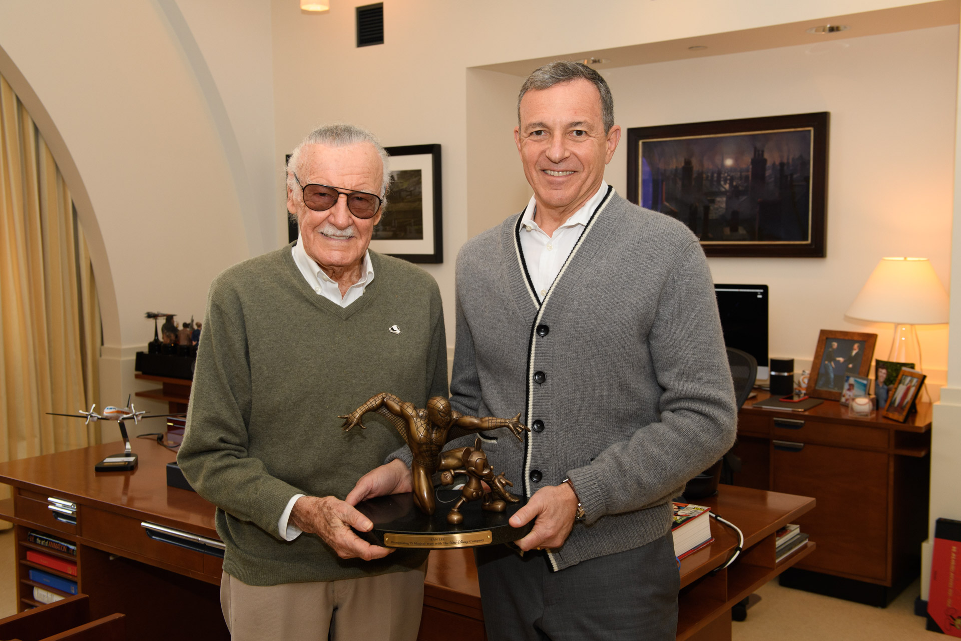 Stan Lee and Bob Iger hold a Spider-Man sculpture together during a meeting in an executive office.
