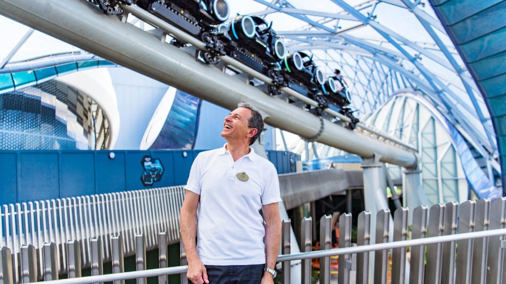 Bob Iger stands beneath the TRON Lightcycle / Run attraction canopy while observing a train passing overhead at Shanghai Disney Resort.