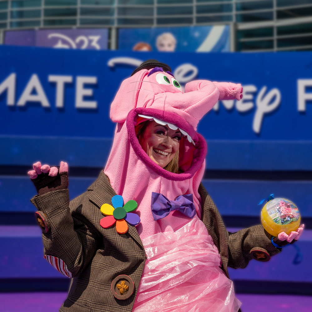 A D23 attendee cosplaying as Bing Bong from Disney and Pixar&rsquo;s Inside Out poses in front of D23: The Ultimate Disney Fan Event signage.