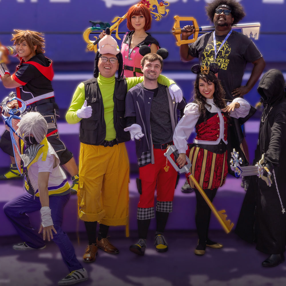 D23 attendees wearing Kingdom Hearts cosplay costumes pose together in front of D23: The Ultimate Disney Fan Event signage
