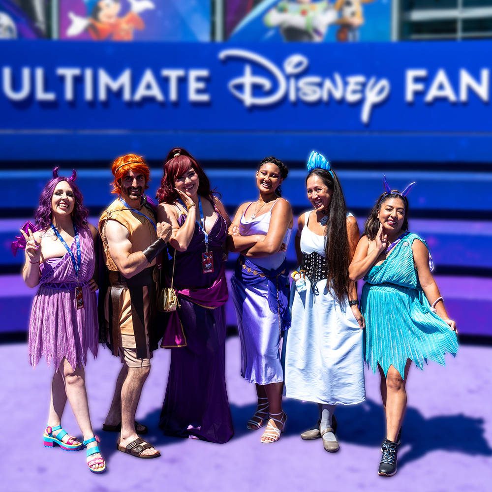 D23 attendees dressed as characters from Disney&rsquo;s Hercules pose together in front of D23: The Ultimate Disney Fan Event signage.