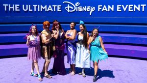 D23 attendees dressed as characters from Disney&rsquo;s Hercules pose together in front of D23: The Ultimate Disney Fan Event signage.