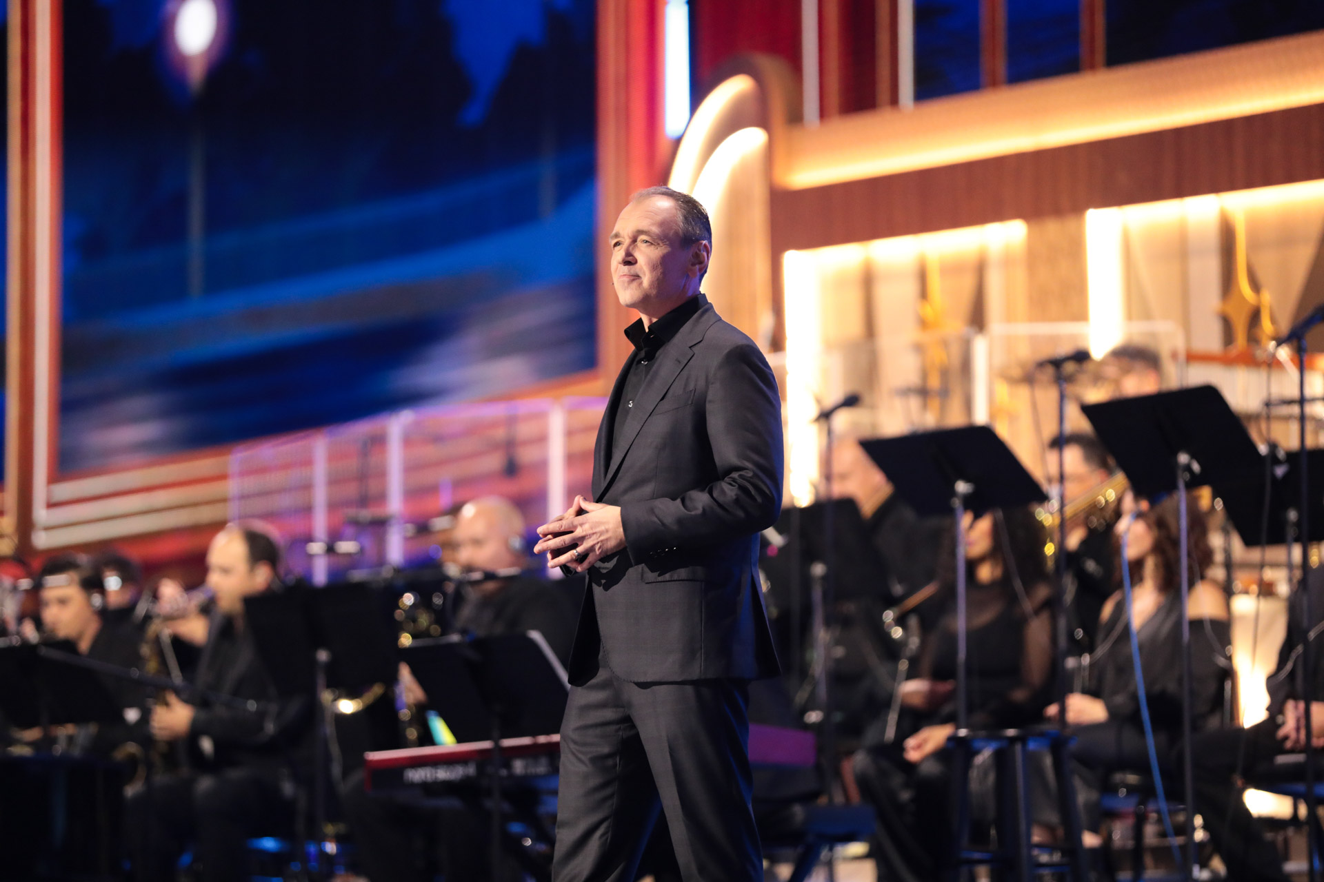 Thomas Mazloum addresses the audience alongside a live orchestra during a Disney Experiences presentation at D23: The Ultimate Disney Fan Event.