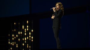 An image of Kathryn Hahn, on stage at the Honda Center during the Disney Entertainment Showcase at D23: The Ultimate Disney Fan Event, telling the crowd about the upcoming live-action Tangled.