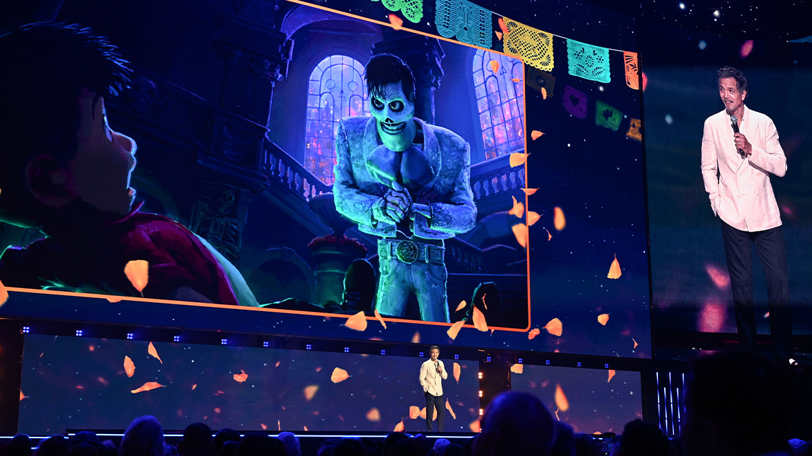 An image of Benjamin Bratt on stage, with an image of Coco 2’s Ernesto de la Cruz in the background, at the Honda Center during the Disney Entertainment Showcase at D23: The Ultimate Disney Fan Event 2026.
