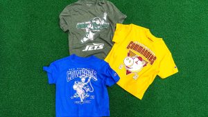 Three youth Disney | Champion NFL T-shirts featuring Buzz Lightyear with the Jets logo, Woody with the Cowboys logo, and a Washington Commanders shirt with Hamm are displayed on green turf.