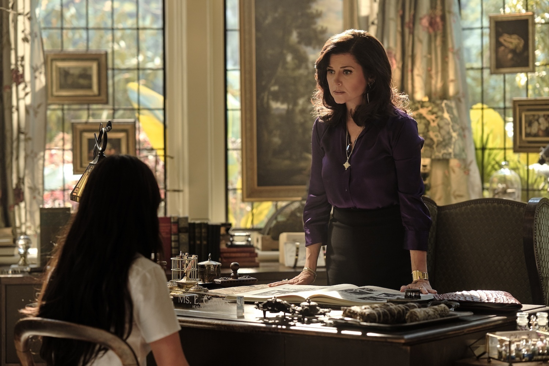 Miss Graves, played by Tiffani Thiessen, stands over her desk while speaking to Briar, played by Malina Weissman, in a scene from Disney&rsquo;s Coven Academy.
