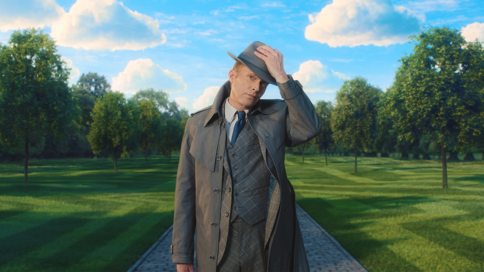 : A man in a trench coat adjusts a hat while standing on a tree-lined path in a scene from VisionQuest.