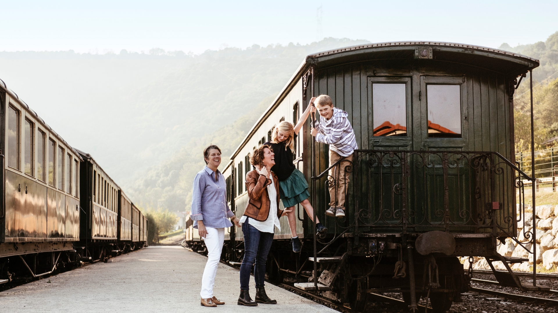 In a promotional image, Adventures by Disney travelers gather beside a historic train carriage at a railway station in the Rh&ocirc;ne region.
