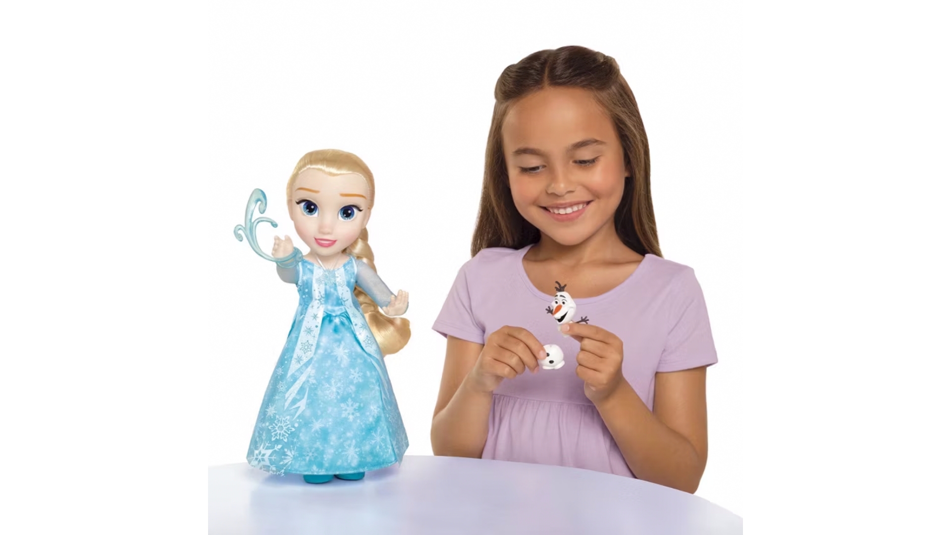 Child holding an Olaf toy figure beside a Frozen-themed Elsa doll on a white tabletop against a plain light background.