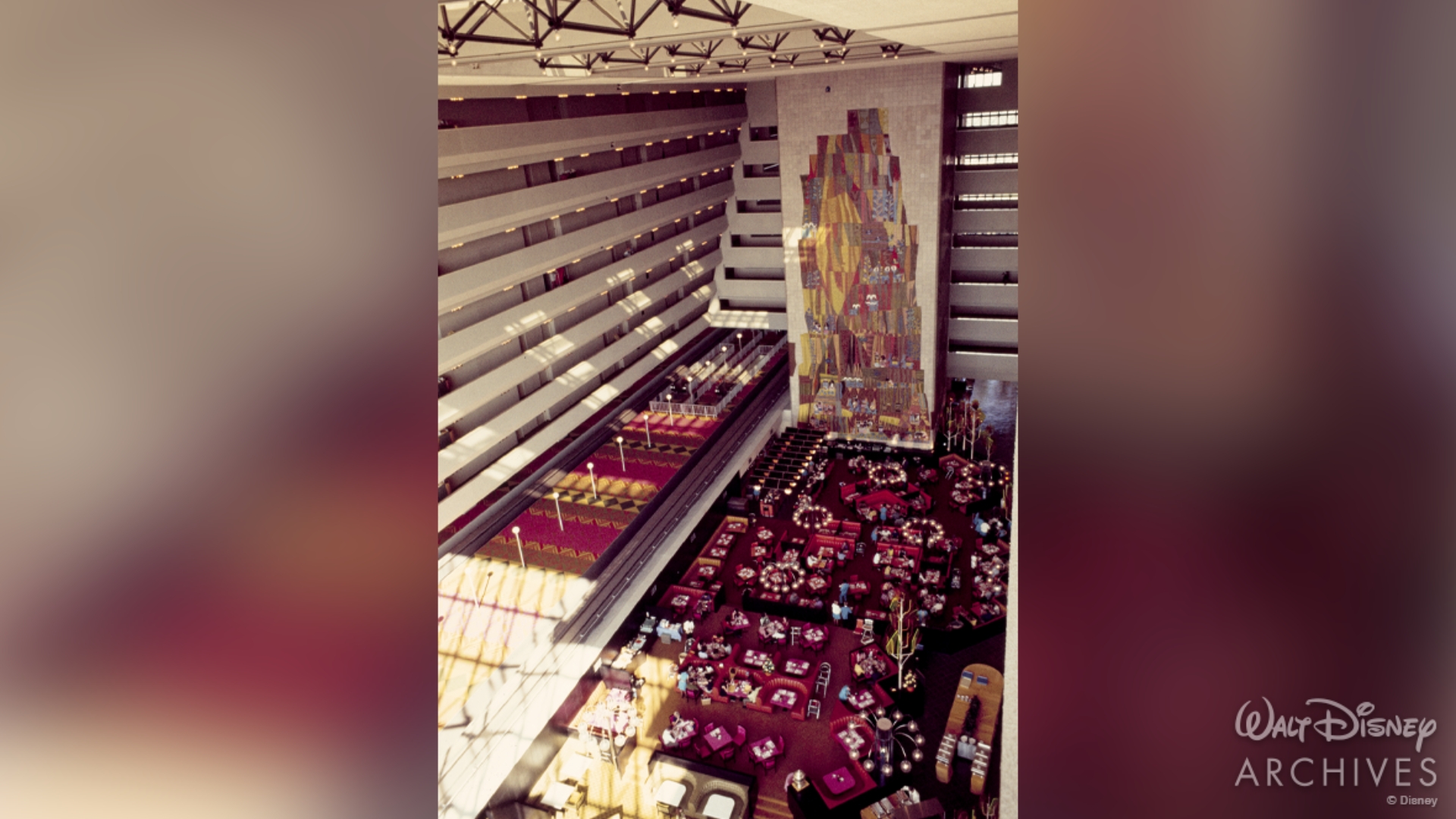 An overhead view of the Grand Canyon Concourse inside Disney&rsquo;s Contemporary Resort. Upscale booths and tables encapsulate the main floor. A large, colorful mural can be seen in full.