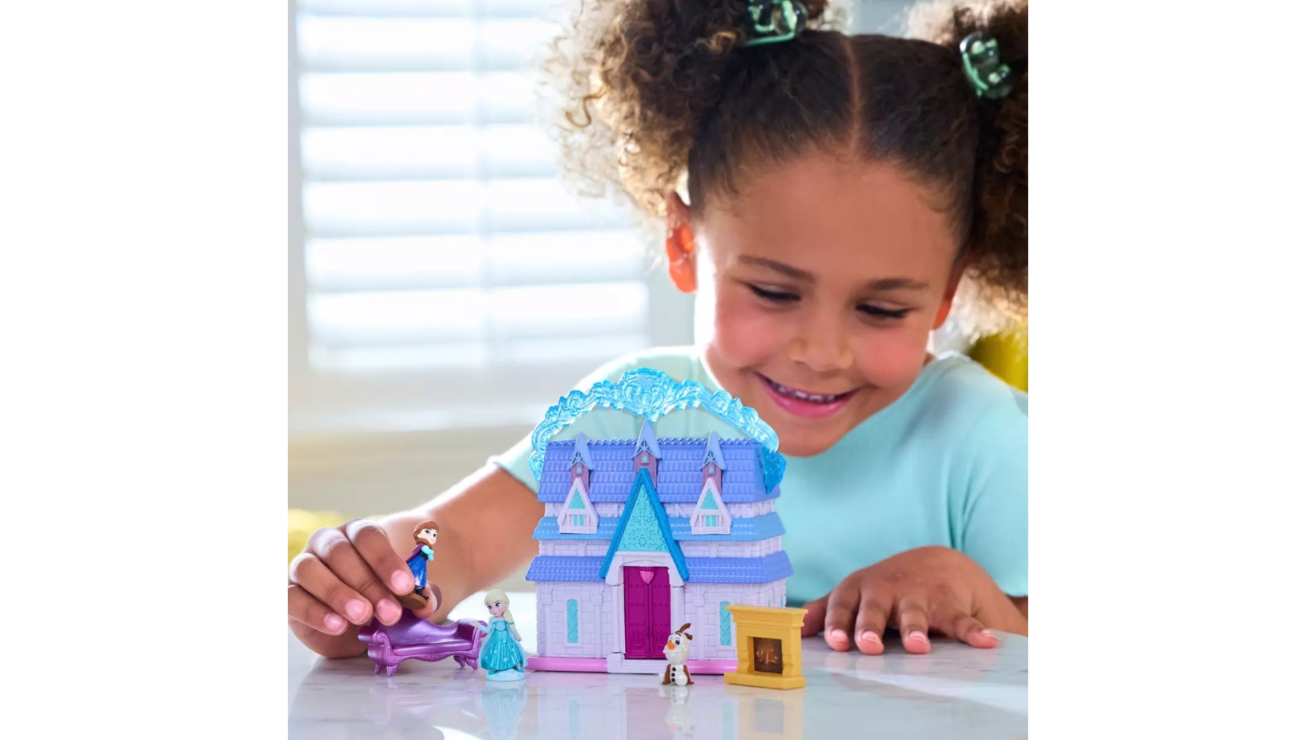 Child playing with a Frozen-themed toy castle and miniature character figures on a tabletop.