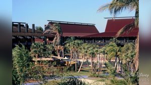 Palm trees fill the foreground of this image of the Great Ceremonial House, Tahiti Longhouse, and Fiji Longhouse, with walking paths winding in between them. Behind, the tall structures of the resort rise right over the tops of the palms.