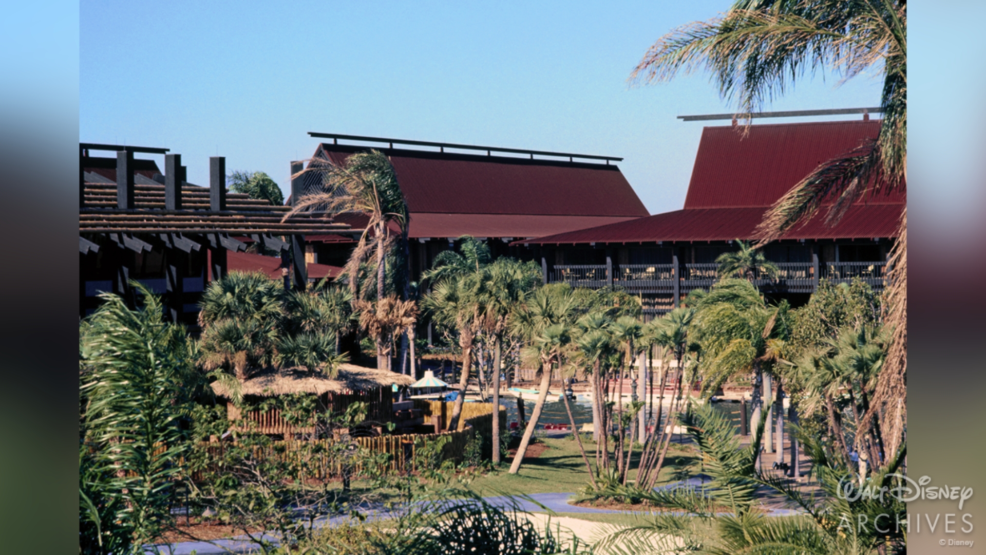 Palm trees fill the foreground of this image of the Great Ceremonial House, Tahiti Longhouse, and Fiji Longhouse, with walking paths winding in between them. Behind, the tall structures of the resort rise right over the tops of the palms.