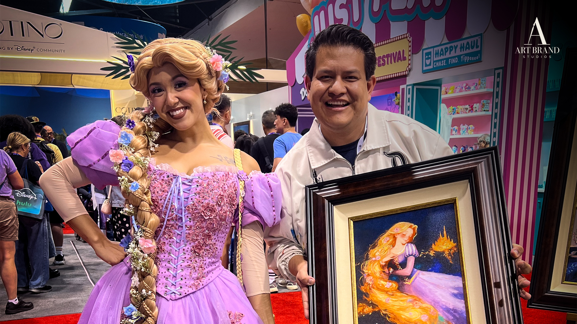 Rapunzel performer and artist pose with a framed Rapunzel painting at D23.