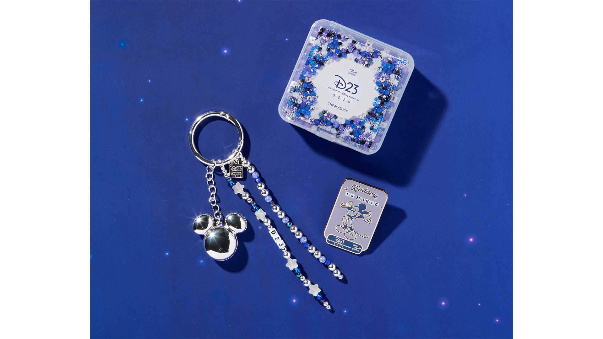 D23 2026 bead kit, Mickey Mouse keychain, and enamel pin displayed on a blue background.