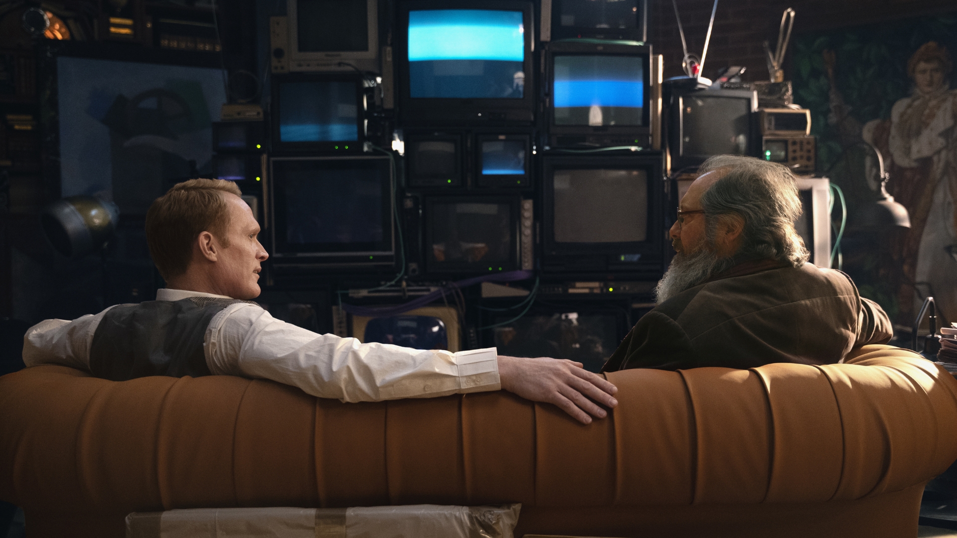 In this scene from Marvel Television&rsquo;s VisionQuest, Vision, played by Paul Bettany, and Ultron, played by James Spader, appear in their human forms. They are seated on a leather couch and face television sets that are stacked on top of and/or beside each other.