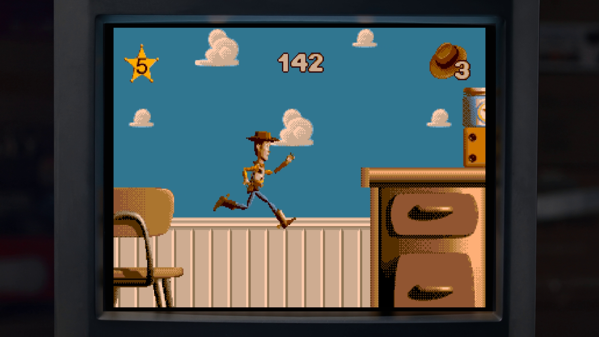 An in-game screenshot showing a Woody running across oversized furniture in Andy's bedroom.