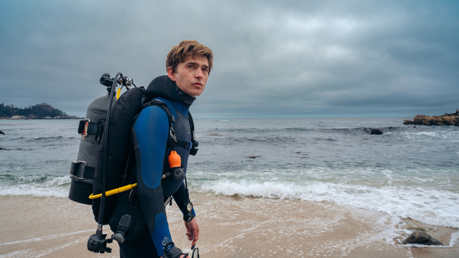 Jay Gardiner, played by Austin Abrams, wears scuba gear and walks along the shoreline in a scene from 20th Century Studios&rsquo; Whalefall.