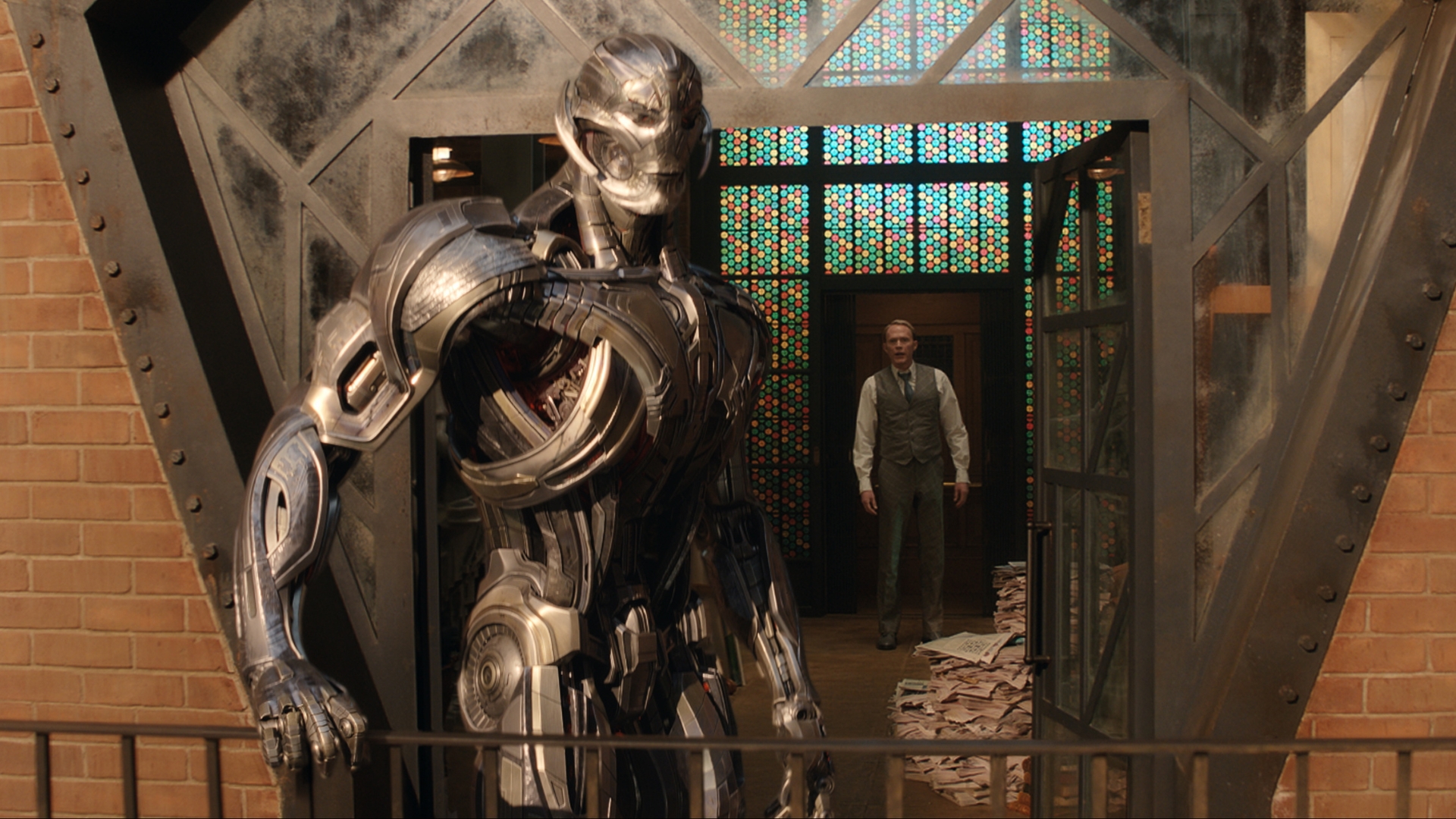 In this scene from Marvel Television&rsquo;s VisionQuest, Ultron, played by James Spader, appears in his robotic form and holds the railing on an outdoor balcony, while Vision, played by Paul Bettany, appears in his human form and stands inside the doorway. 