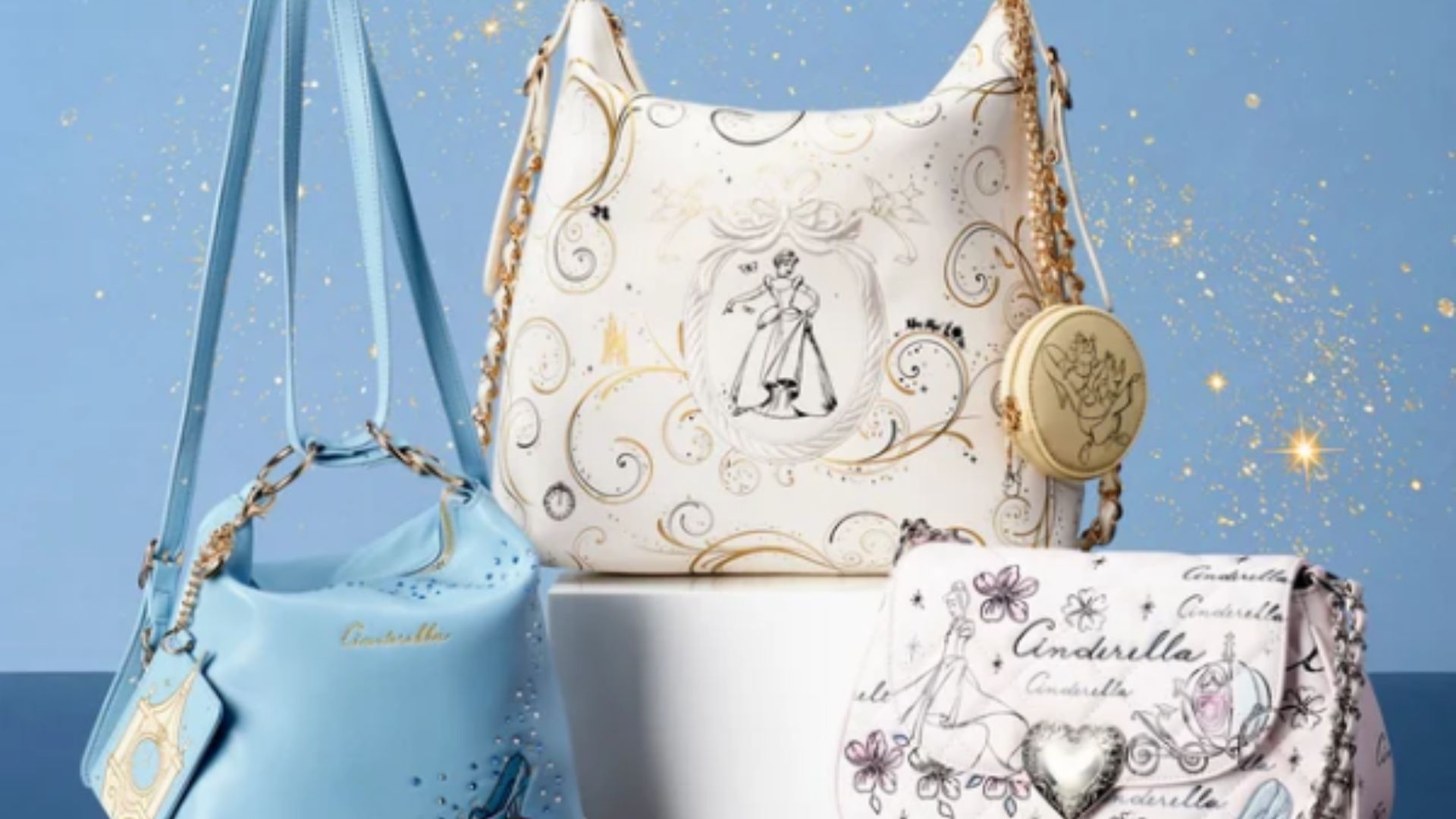 The Cinderella collection includes 3 bags all on display. The first is a large bag with an outline drawing of Cinderella and gold-colored trimming around the bag. The second is a blue bag which features the iconic glass slipper surrounded by sparkles. The third is a light pink bag that features an outline of Cinderella, the pumpkin carriage, the glass slipper and other flowers. 