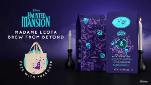 Promotional image for Disney Haunted Mansion themed coffee. Against a dark purple, misty background, two lit white candles flank purple coffee bags branded &ldquo;Joffrey&rsquo;s Coffee & Tea Company&rdquo; and &ldquo;Disney Haunted Mansion: Madame Leota Brew From Beyond.&rdquo; The packaging features teal and purple artwork with skulls, vines, and an illustration of Madame Leota. Large text reads &ldquo;Haunted Mansion&rdquo; and &ldquo;Madame Leota Brew From Beyond.&rdquo; In the lower left, a cream-colored tote bag with a purple sorcerer-style hat graphic is shown with text indicating it is free with purchase. The product is identified as medium roast coffee, 11 oz (312 g). Disney copyright appears in the bottom-right corner.